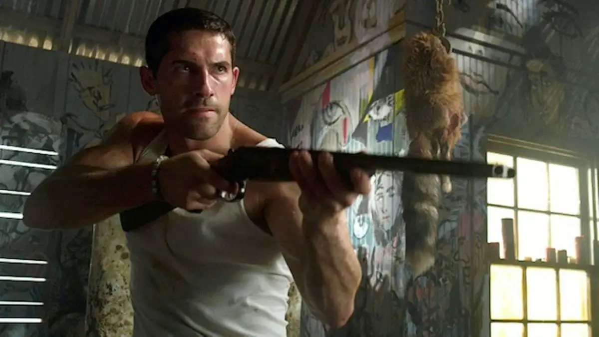 Current low budget action king Scott Adkins holds a shotgun in a warehouse