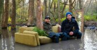 Justin Benson and Aaron Moorhead sit on a sofa in a swamp on the set of Syncronic