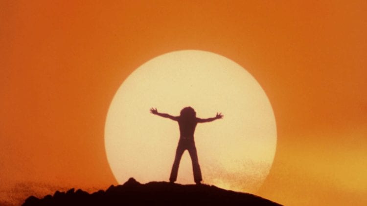 Silhouette of Tommy on a mountaintop, raising his arms against the sun