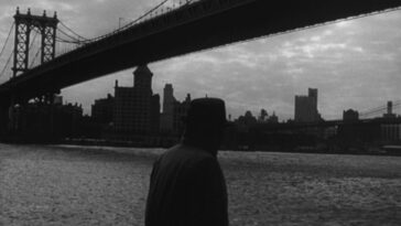 Still from Blast of Silence. Frankie Bono walks in front of a NYC bridge, silhouetted by the city skyline.