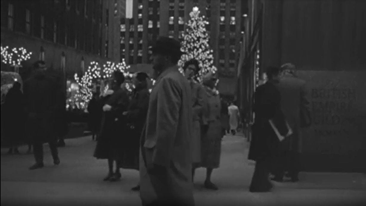 Still from Blast of Silence. Frankie Bono walks past the tree at Rockefeller Center. He is wearing a trench coat and looking very purposefully forward, as if ignoring the tree to his right.