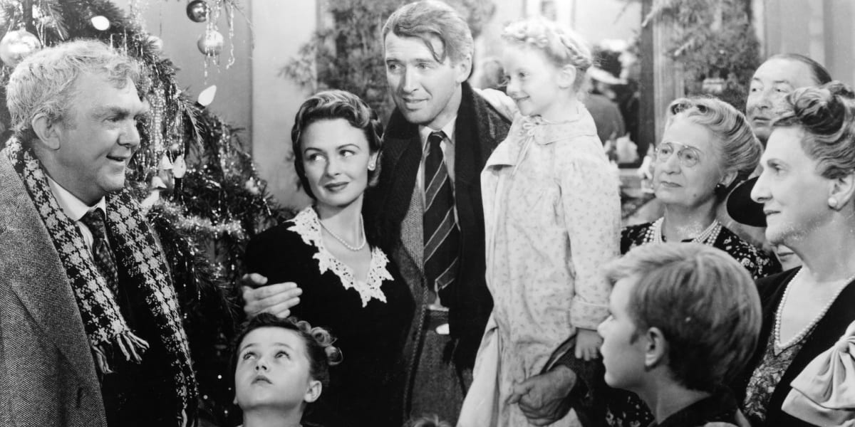 George Bailey surrounded by his friends and family, with a Christmas tree to his left, in black and white photo from It's A Wonderful Life