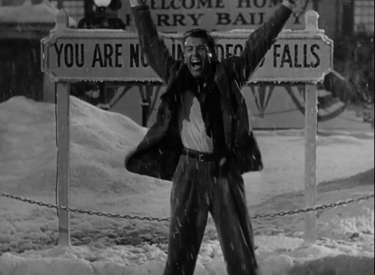 George Bailey stands triumphant in front of Bedford Falls sign