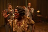 Ma Rainey sings into a recording microphone in front of her band.