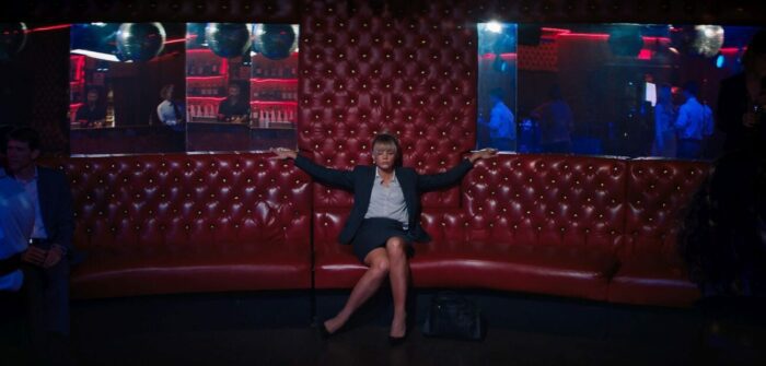 Cassie sits on a club couch provacatively.