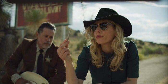 Elsa examines a piece of evidence wearing a hat and sunglasses next to the sheriff.