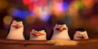 Penguins of Madagascar screenshot featuring, from left to right, Kowalski, Skipper, Rico, and Private. All bare serious expressions, save for Rico, who looks a bit disgusted, just having coughed up a pile of sand. They are peeking out of a manhole cover in front of many colorful lights, blurred to the point of being hardly distinguishable from anything else sparkly.