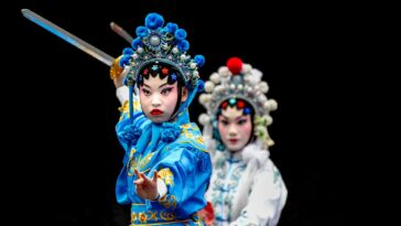 Two actors in traditional Chinese Opera costumes stand one in front of the other with their swords raised.
