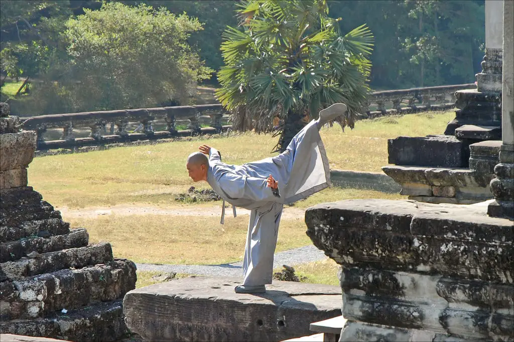 A MArtial Artist stands on one leg, with his other stretched out behind him, on a tone wall of Angkor Wat