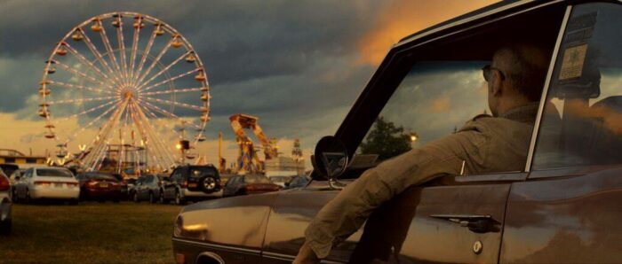 Charlie watches a carnival while in his car.