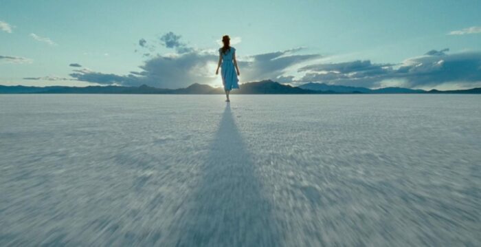 A woman walks on a salt flat on a partly cloudy day.