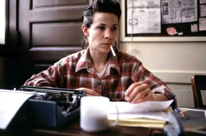 Valerie Solanas (Lili Taylor) sits at a desk covered in papers, a typewriter to her right. She is smoking a cigarette