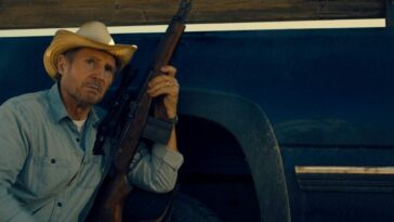 Liam Neeson hunches down next to a truck with his rifle