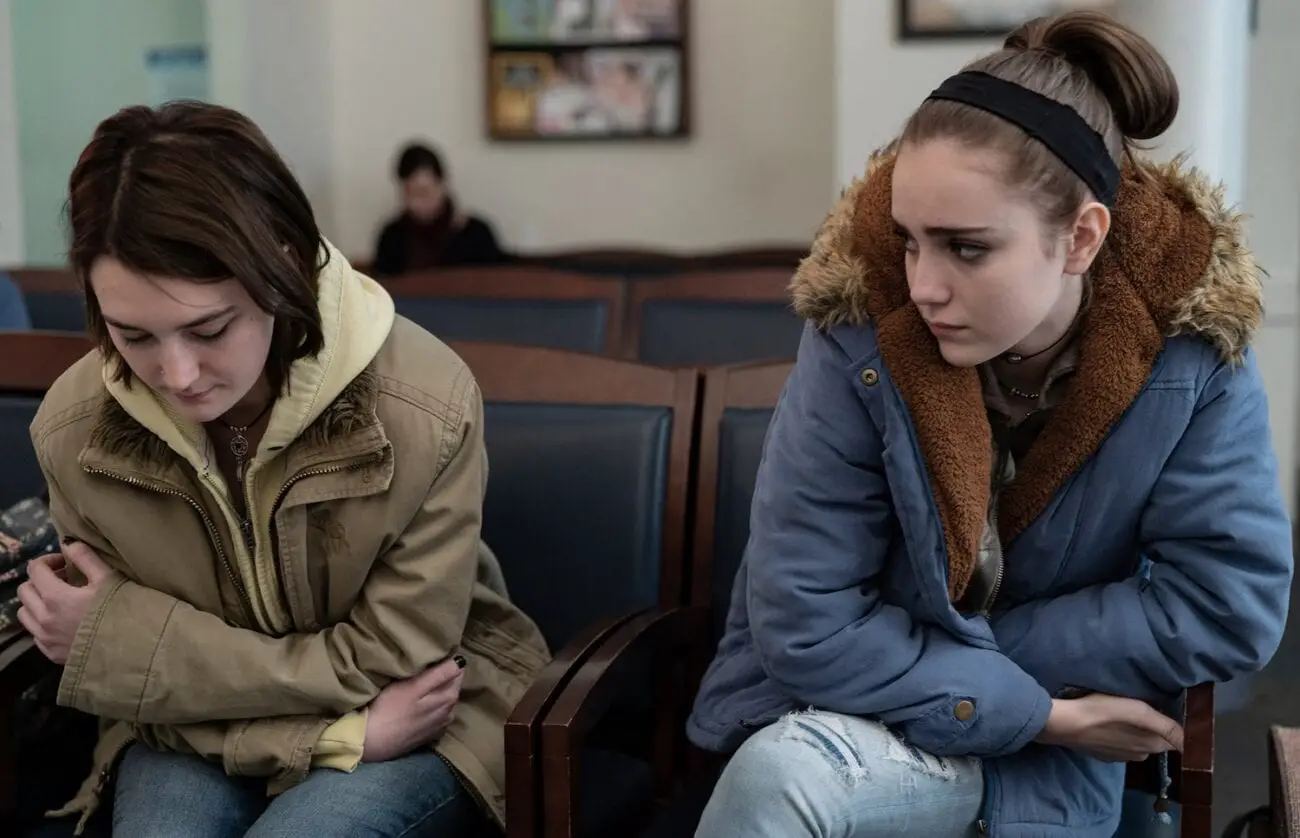 Sidney Flanigan's Autumn sits pensively in a waiting room as her cousin Skylar, played by Talia Ryder looks on sympathetically; Never Rarely Sometimes Always, Focus Features 2020 LLC