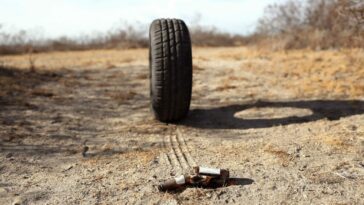 a tire rolls down a dirt road toward an empty beer bottle