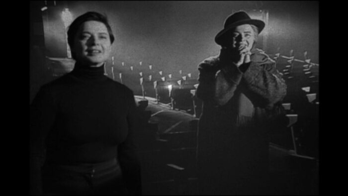 Still from My Dad is 100 Years Old. Actress Isabella Rossellini portrays herself and director Frederico Fellini (right). Rossellini is wearing a black turtleneck, "Fellini" a hat, coat, and scarf. They both look pleased and excited