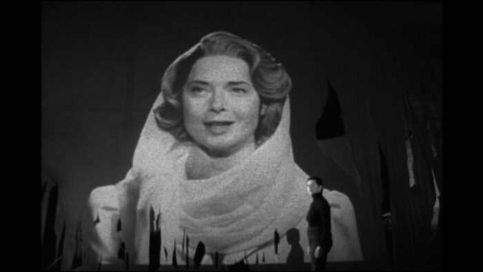 Still from My Dad is 100 Years Old. Isabella Rossellini plays her real-life mother, Ingrid Bergman, as she is projected on a large screen. In front of her is the real Rossellini, looking off to the side.