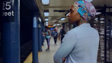 Still from a newly added short film on the Criterion Channel. Actress Chinasa Ogbuagu plays Kamara in On Monday Last Week. She is standing waiting for a subway. She is standing with her arms casually crossed and her back is slightly turned towards the camera.
