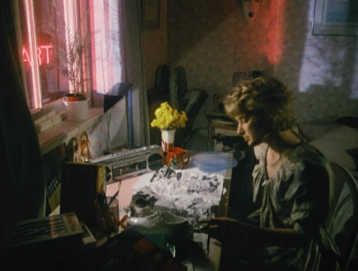 The woman sites by her table near a window at night, reading a crumpled newspaper.