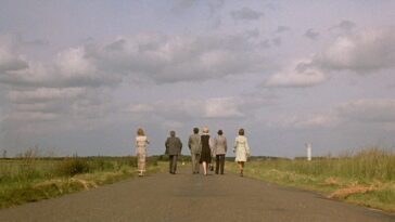 A long-shot behind the backs of the main characters as they walk along a road in the countryside