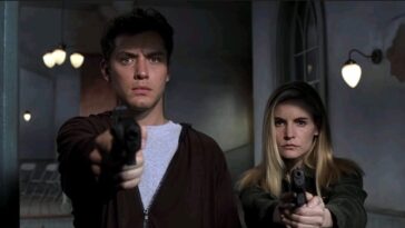 A close-up shot of Ted Pikul (Jude Law) and Allegra Geller (Jennifer Jason Leigh) aiming their handguns towards the camera