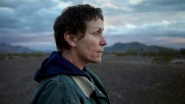 Frances McDormand stares into open space, surrounded by mountains and dirt roads