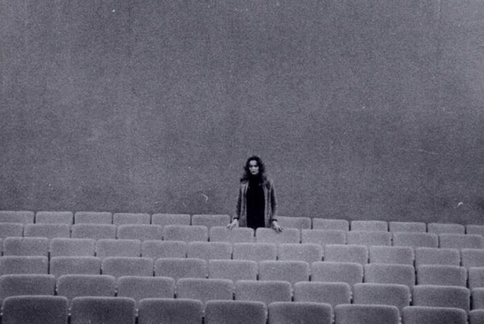 Eliane Radigue stands by herself in an auditorium.