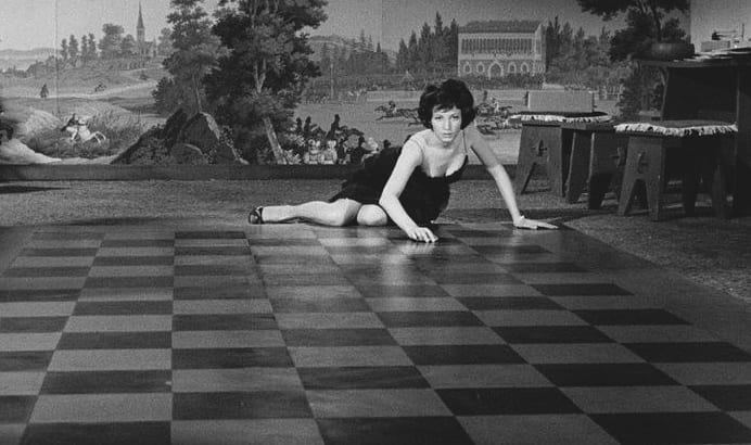 Vaneltina lies across a large checkered floor getting read to slide her compact along the tiles