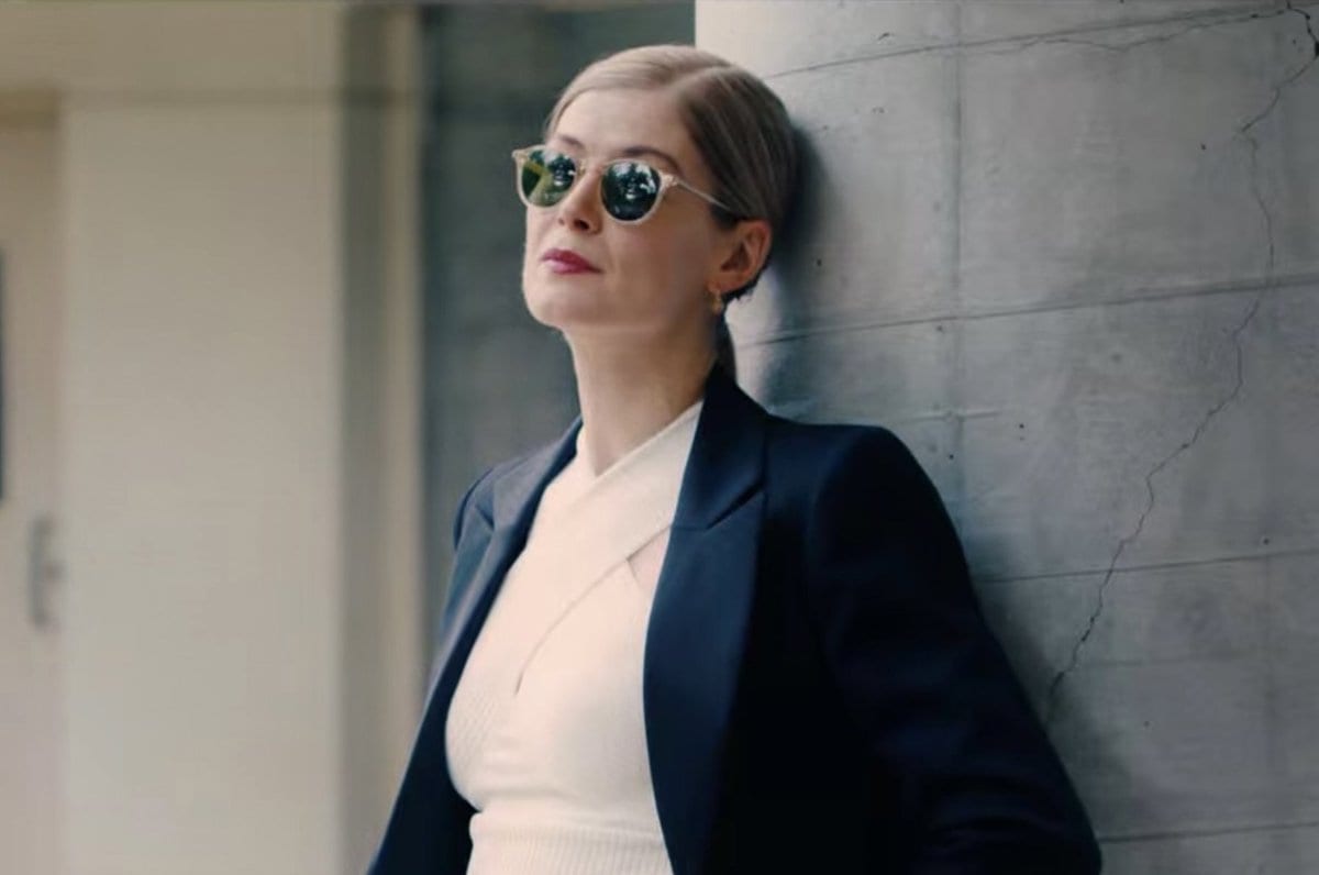Marla Grayson, wearing sunglasses and a snazzy business suit, leans on a wall outside of the courtroom: emanating cool.