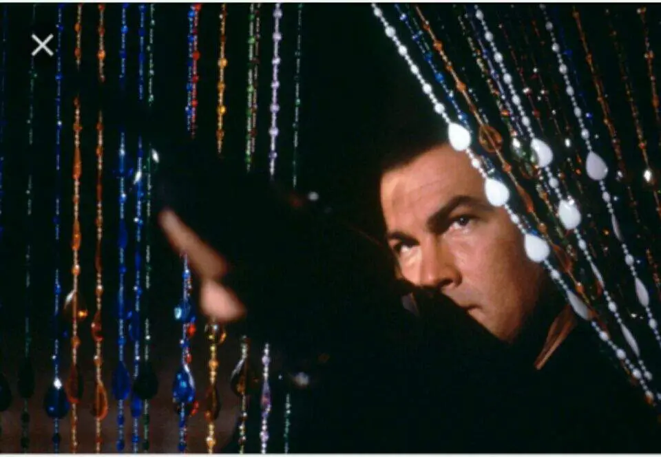 Gino emerging from a wall of beads, point a shotgun