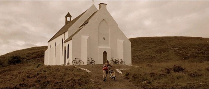 A white church sits surrounded by grass and a hill behind it, with bicycles out front
