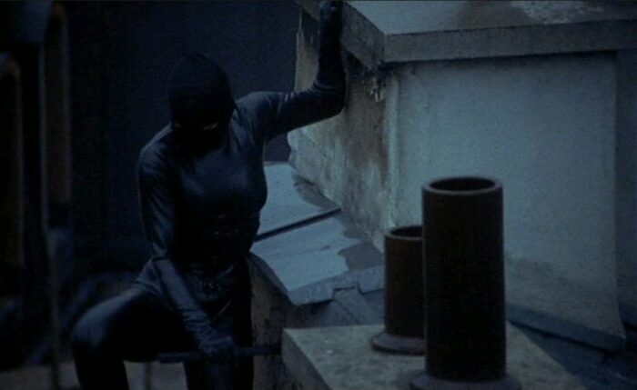 A medium shot of Maggie Cheung climbing a rooftop in her Irma Vep burglar outfit