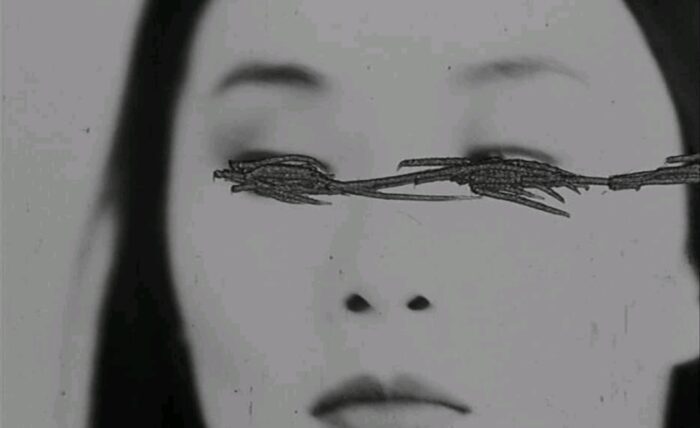 A close-up black and white shot of Maggie Cheung's faces her eyes have scratch marks within the film image.