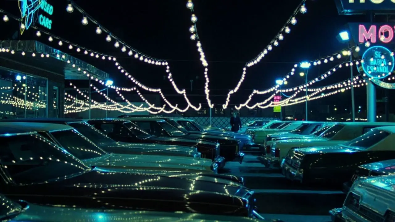 Frank walking through a car lot with lights above
