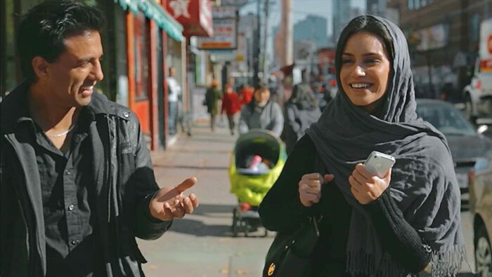 Ethan and Sahar smile as they walk down a street in Toronto