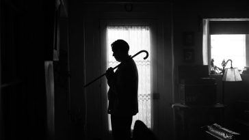 Mank standing in silhouette with a cane on his shoulder