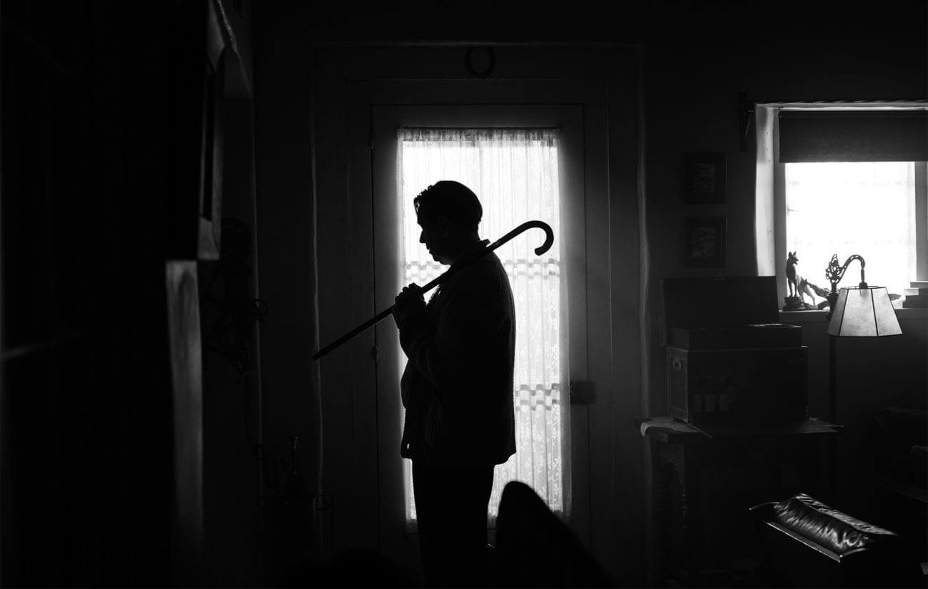 Mank standing in silhouette with a cane on his shoulder