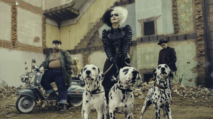 Cruella holds three leashed dalmatians in front of her sitting two friends.