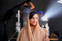 Nayla Al Khaja stands smiling while a film light shines behind her
