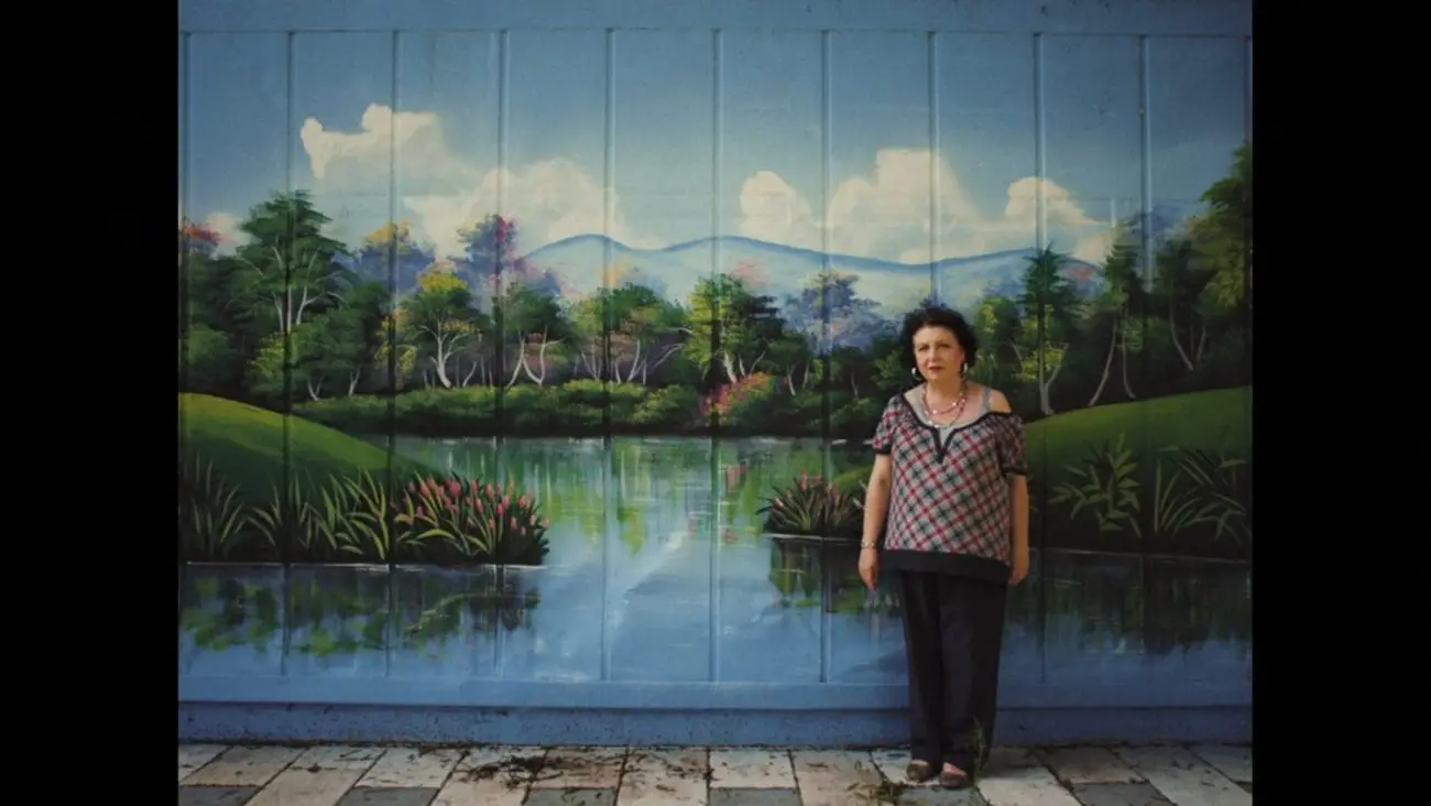 A woman stands in front of a mural depicting a pastoral landscape.