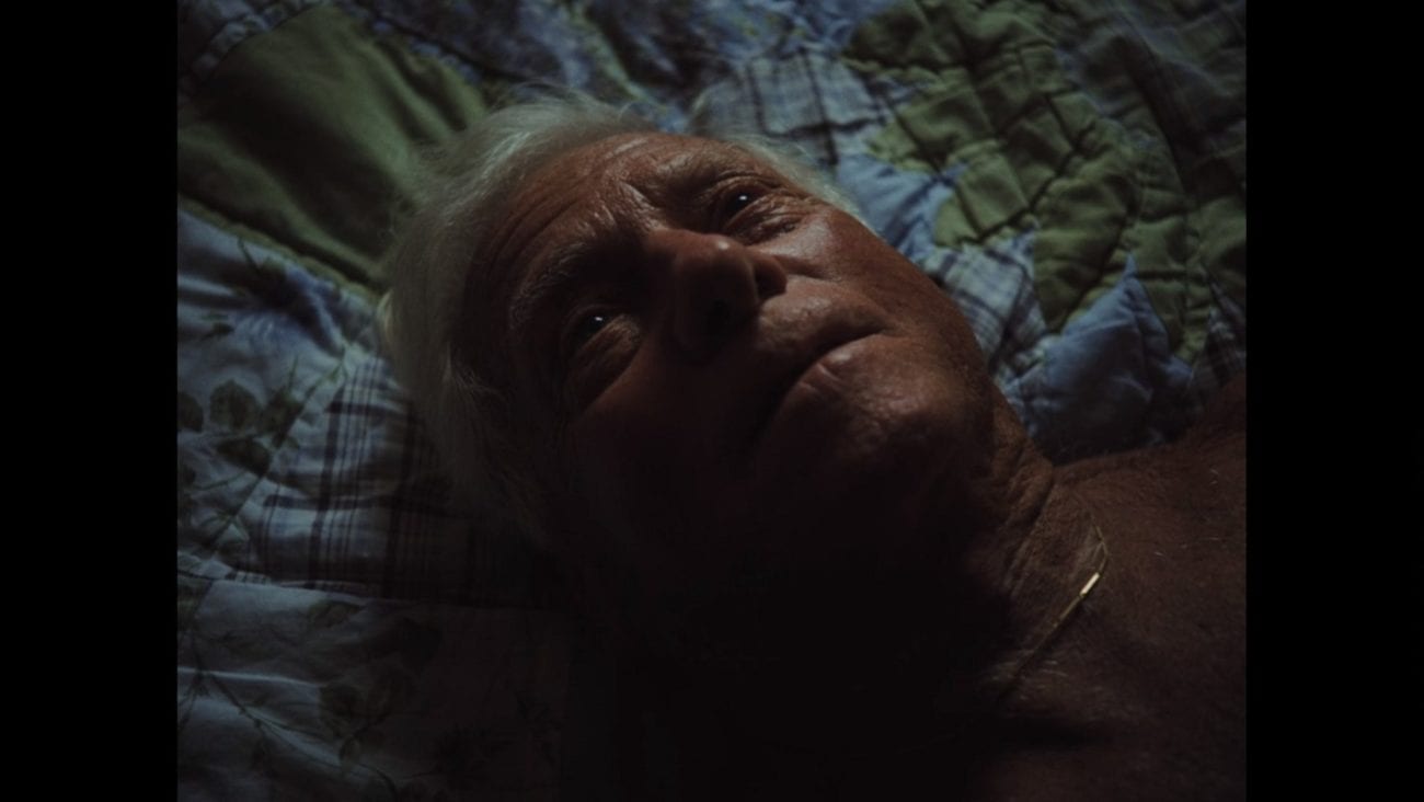 An elderly man lies on a bed gazing upwards.