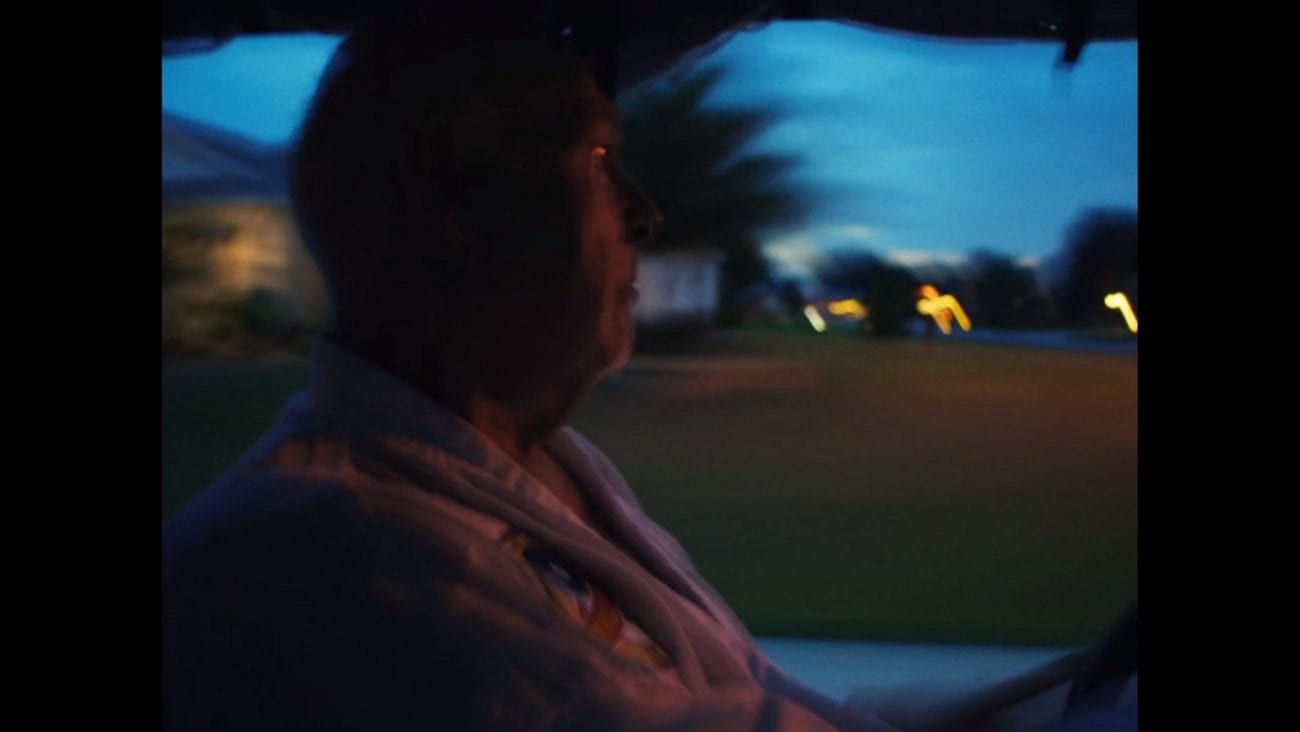 A blurred image of an older man driving a golf cart at dusk.