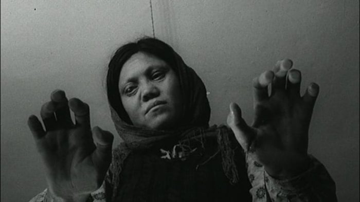 Still from The House is Black. A woman with leprosy looks at her hands on top of a glass table.