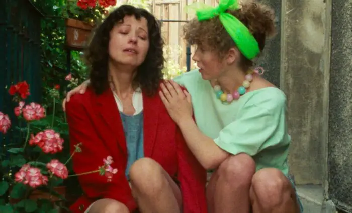 Delphine crying on a stoop as her friend comforts her.