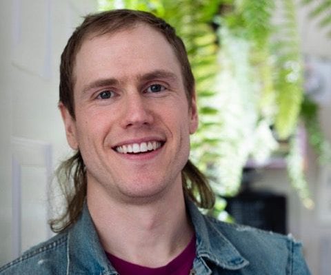 Conor Stechschulte, writer of Ultrasound, smiles. Clean-shaven, his hair is short in the front and long in the back down each side. He is wearing a denim jacket with a collar
