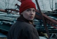 In this image from Nicole Riegel's Holler, the character Ruth (played by Jessica Barden) stands in front of scrap metal and stares at the camera.