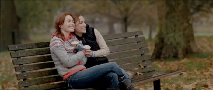 Luce (Lena Headey) and Rachel (Piper Perabo) snuggle close on a bench to keep warm.