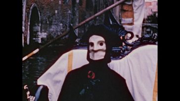 Still from The Assignation. The masked personification of death rides in a gondola in Venice. He is holding a rose.