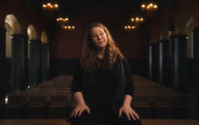 Opera performer Lucia Lucas crouches on a stage in front of rows of empty concert seats