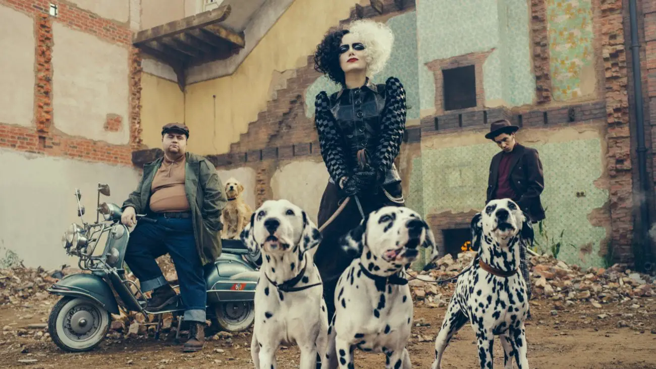 Cruella holds three Dalmatians on a leash while her cohorts stand nearby